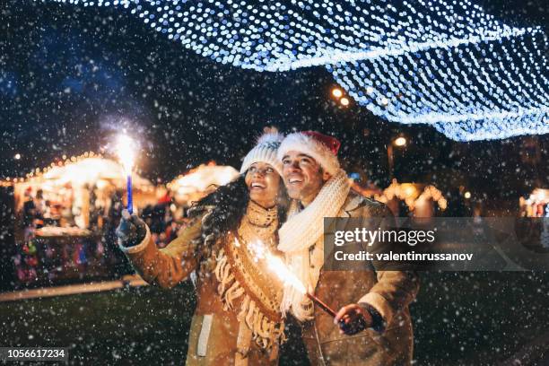 young couple having fun with sparkling candles at night - woman snow outside night stock pictures, royalty-free photos & images