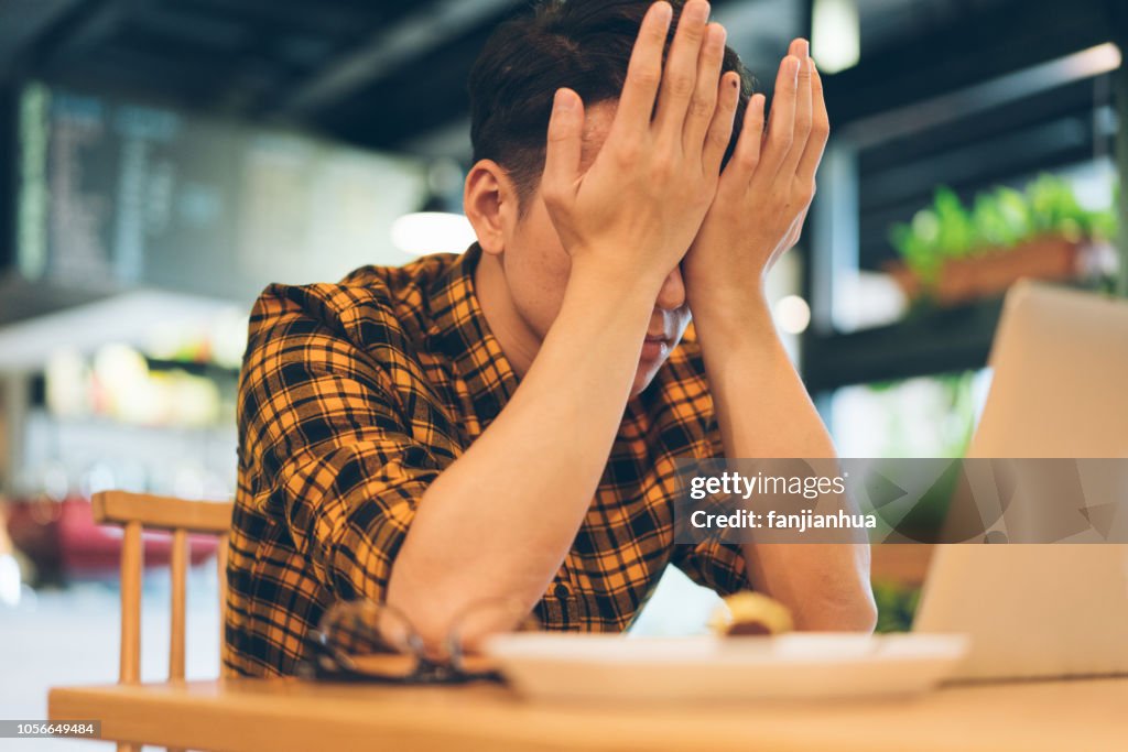 Exhausted young man rubbing eyes in cafe