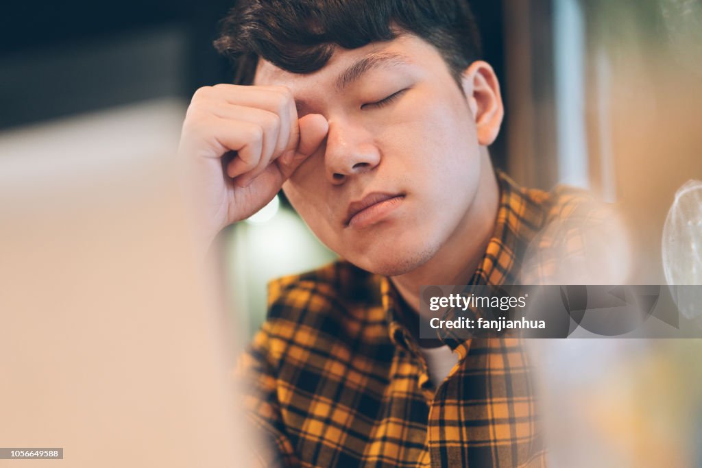 Exhausted young man rubbing eyes in cafe