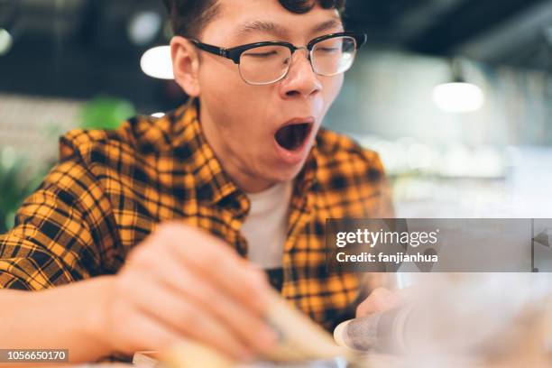 young man yawning while reading - yawning stock photos et images de collection