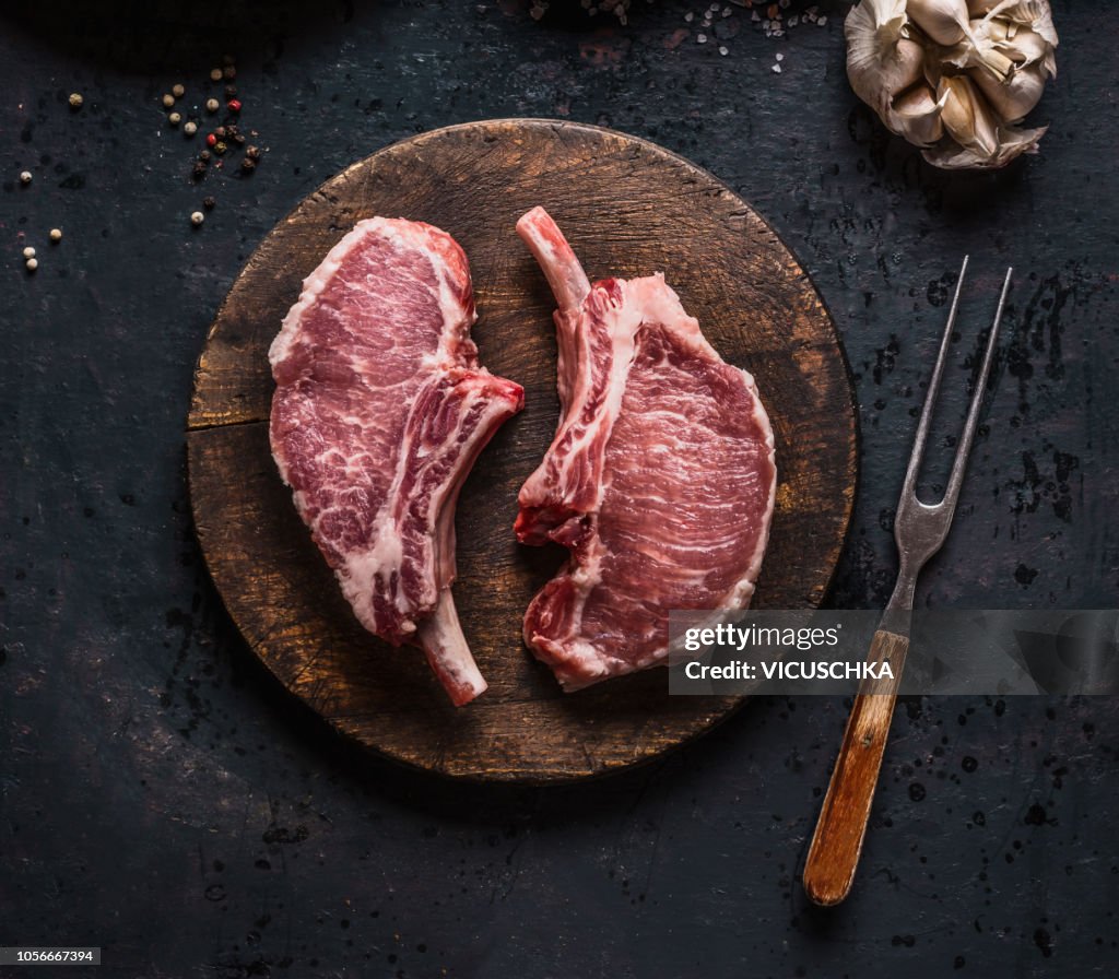 Marbled raw pork chops of Porco Iberico meat on round cutting board with meat knife. French Racks