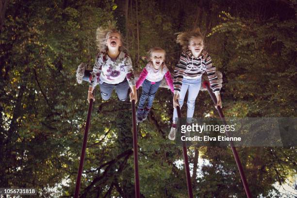upside down image of three girls having fun on a rope swing in a forest playground - quirky family stockfoto's en -beelden