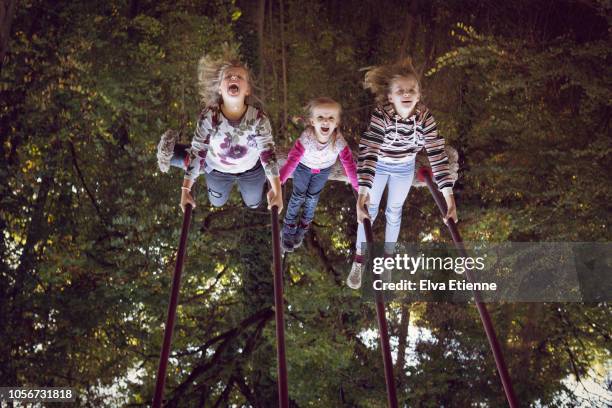 upside down image of three girls having fun on a rope swing in a forest playground - playground swing stock pictures, royalty-free photos & images