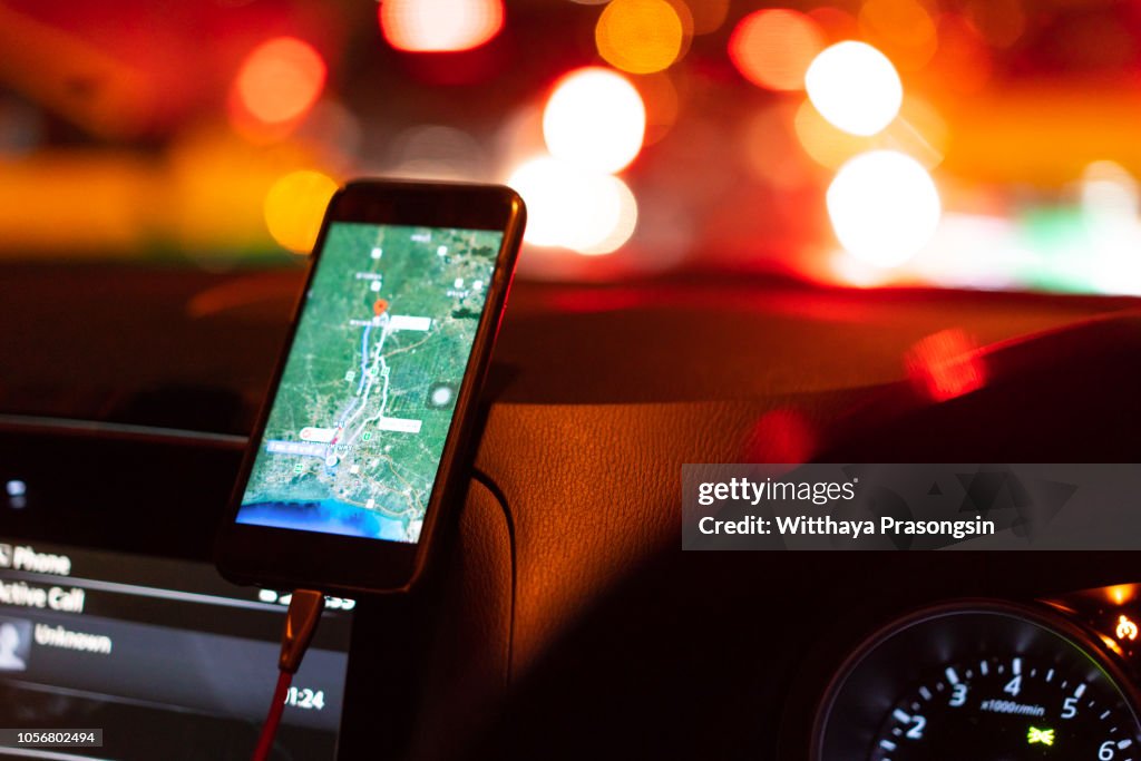 The map on the phone in the background of the dashboard. Black mobile phone with map gps navigation fixed in the mounting. App map for travel.