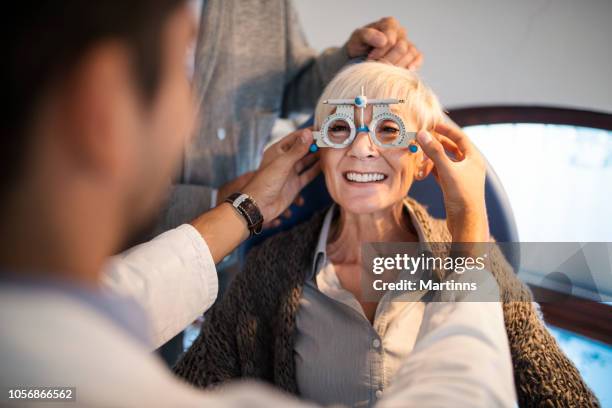 young smiling ophthalmologist checking eyesight of an old woman. - male eyes stock pictures, royalty-free photos & images