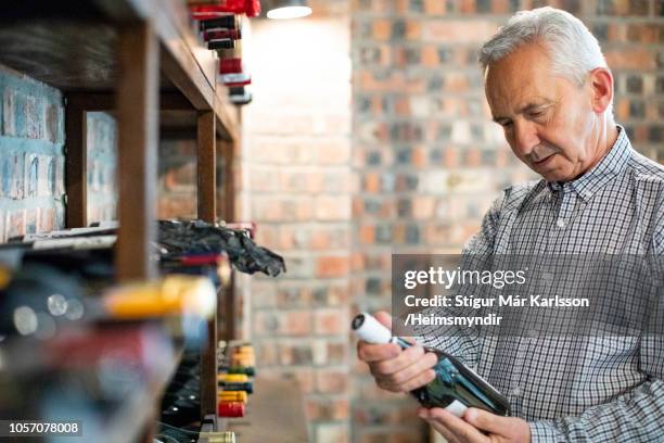 senior man standing by rack holding wine bottle - wine rack stock pictures, royalty-free photos & images