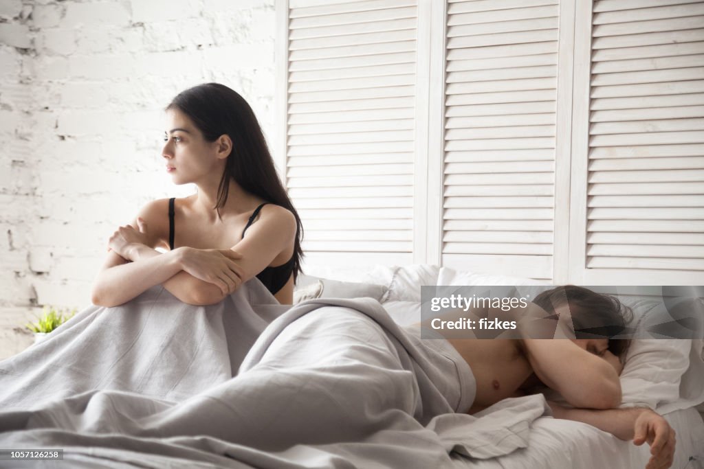 Sad woman and sleeping man lying in bed