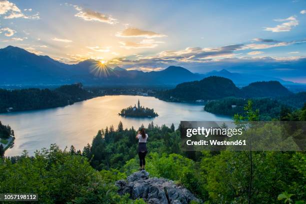 slovenia, bled,  young woman taking picture of bled island and church of the assumption of maria at sunrise - bled slovenia stock pictures, royalty-free photos & images