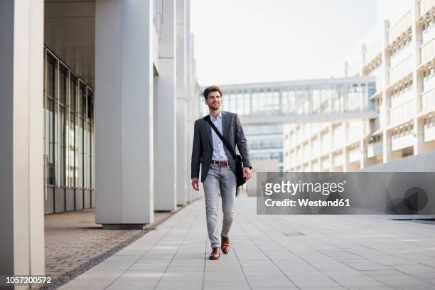 smiling businessman with crossbody bag in the city on the move - gehen stock-fotos und bilder