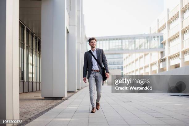 smiling businessman with crossbody bag in the city on the move - business man walking photos et images de collection