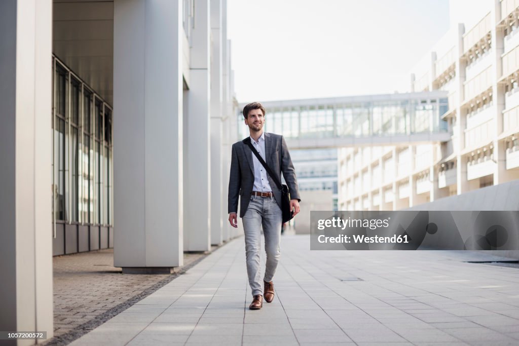 Smiling businessman with crossbody bag in the city on the move
