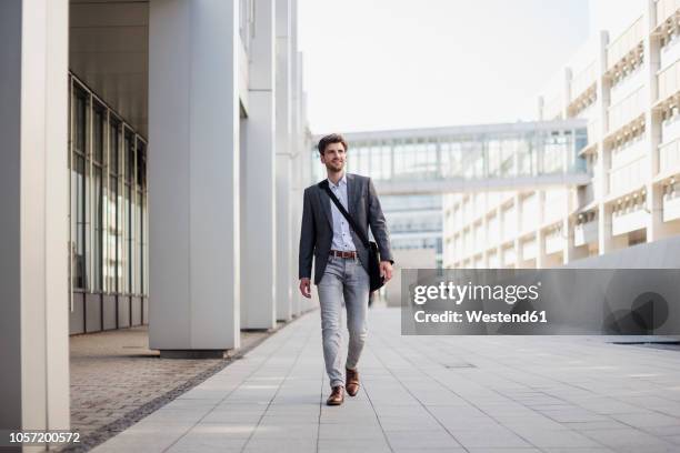 smiling businessman with crossbody bag in the city on the move - andar imagens e fotografias de stock