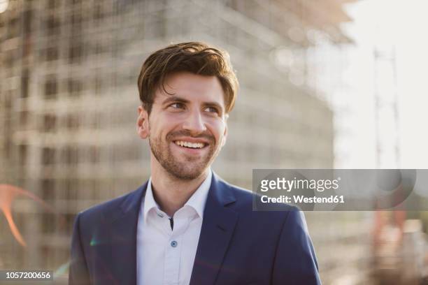 portrait of smiling businessman in front of construction site looking sideways - men suit light stock pictures, royalty-free photos & images