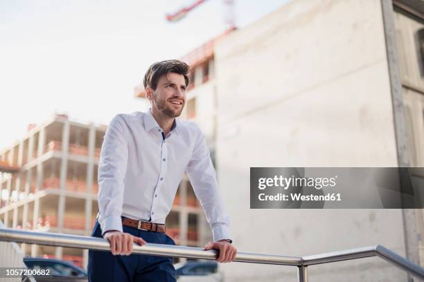 portrait of smiling businessman in the city leaning on railing - bauherr stock-fotos und bilder