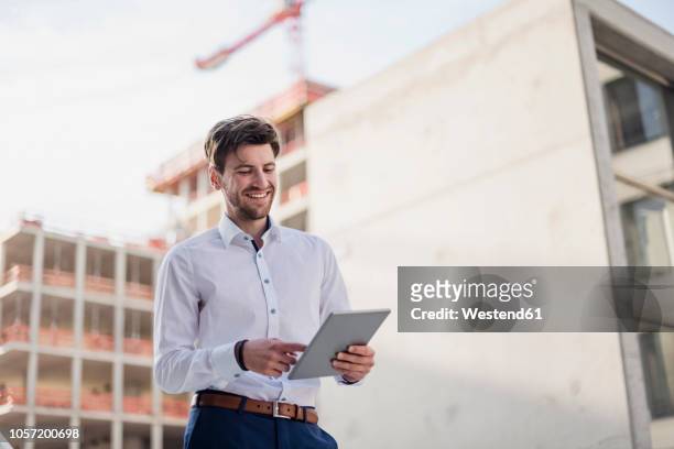 smiling businessman in the city using tablet - businesswear stock pictures, royalty-free photos & images