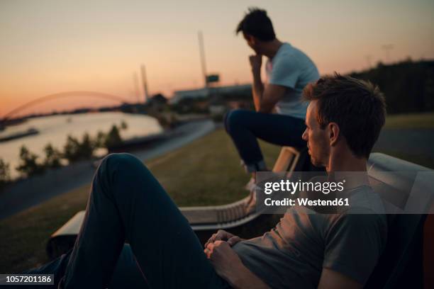 two friends watching sunset at the river - riverbank stock-fotos und bilder