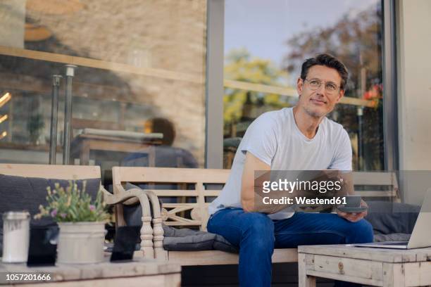 mature businessman sitting in coffee shop, drinking coffee, using laptop - outdoor cafe stock-fotos und bilder