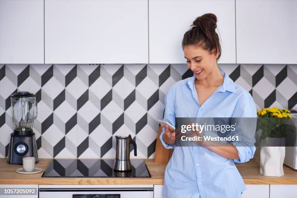 young woman preparing coffee in the morning, using smartphone - woman cooking phone stock-fotos und bilder