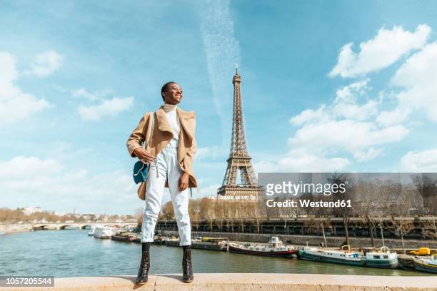 france, paris, smiling woman standing on a bridge with the eiffel tower in the background - paris tourist stock pictures, royalty-free photos & images