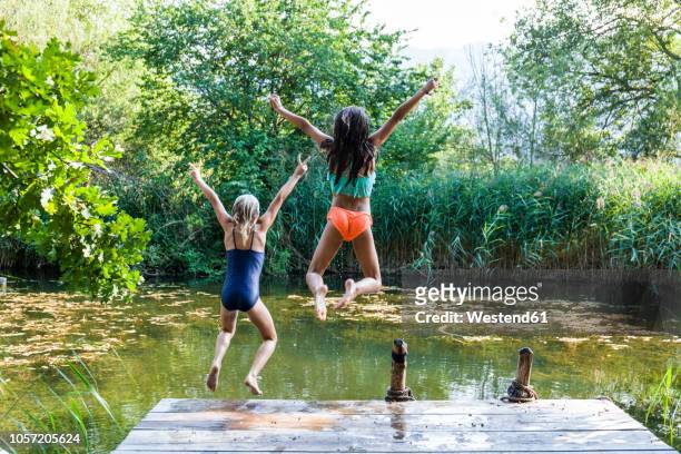 two carefree girls jumping into pond - bathing jetty stock pictures, royalty-free photos & images