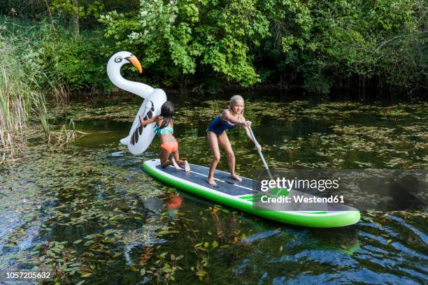 two girls in a pond with inflatable pool toy in swan shape and sup board - pond stock pictures, royalty-free photos & images