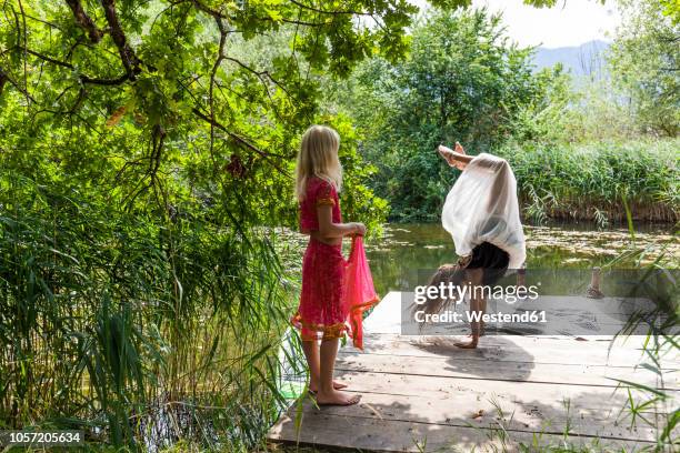 girl on jetty at a pond watching friend doing a handstand - girl in dress doing handstand stockfoto's en -beelden