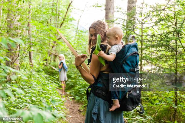Woman hiking in the woods showing large leaf to baby boy in backpack