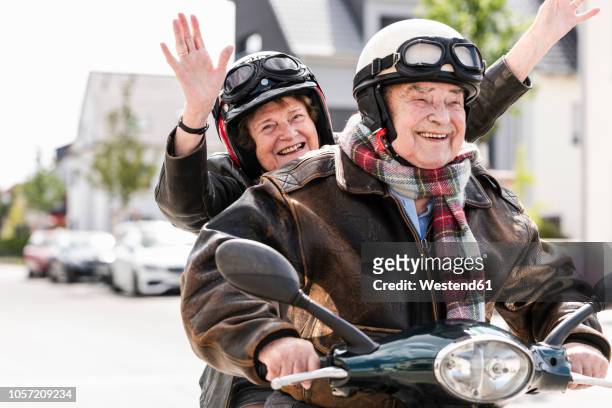 happy senior couple having fun, riding motor scooter and waving - old couple adventure stock-fotos und bilder