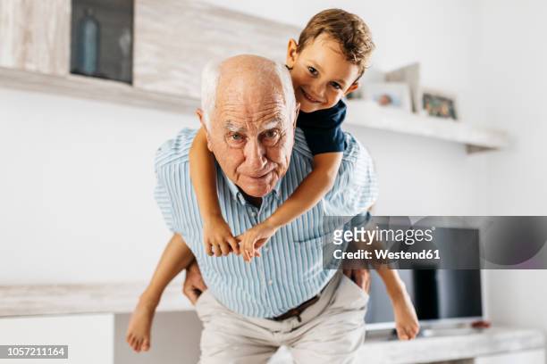 portrait of grandfather giving his grandson a piggyback ride in the living room - abuelos fotografías e imágenes de stock