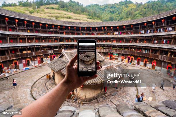 china, fujian province, hand taking cell phone picture of the inner courtyard of a tulou in a hakka village - fujian province - fotografias e filmes do acervo