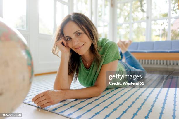 smiling mature woman lying on the floor at home with globe - frau globus stock-fotos und bilder