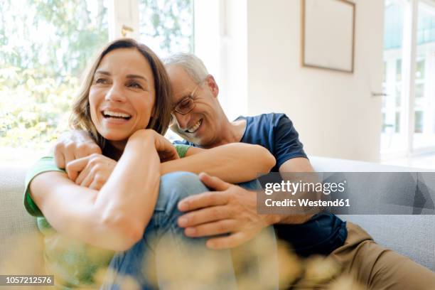 happy mature couple sitting on couch at home - couple laughing hugging stockfoto's en -beelden