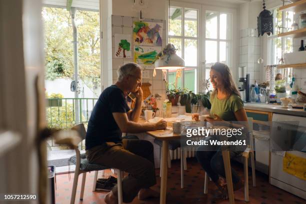 mature couple sitting at kitchen table at home - woman drinking phone kitchen stockfoto's en -beelden