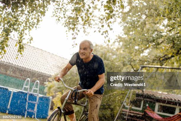 happy mature man riding bicycle in summer rain in garden - velofahren stock-fotos und bilder