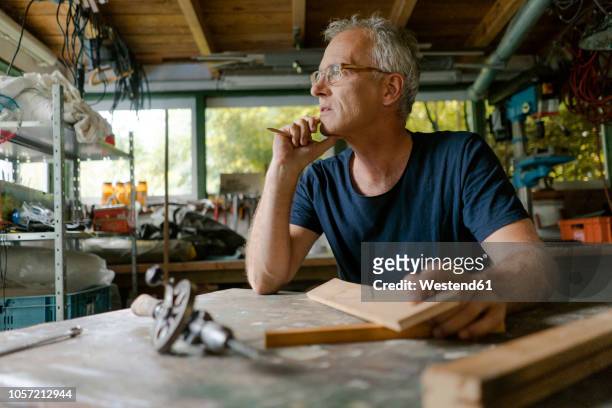 mature man at workbench in his workshop thinking - wood worker posing stock-fotos und bilder