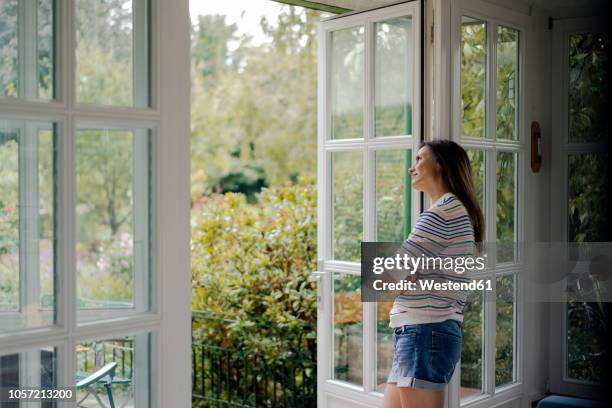 mature woman looking out of terrace door at home - french doors stockfoto's en -beelden