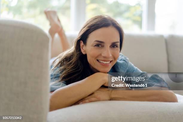 portrait of smiling mature woman lying on couch at home - beautiful woman 40s stock pictures, royalty-free photos & images