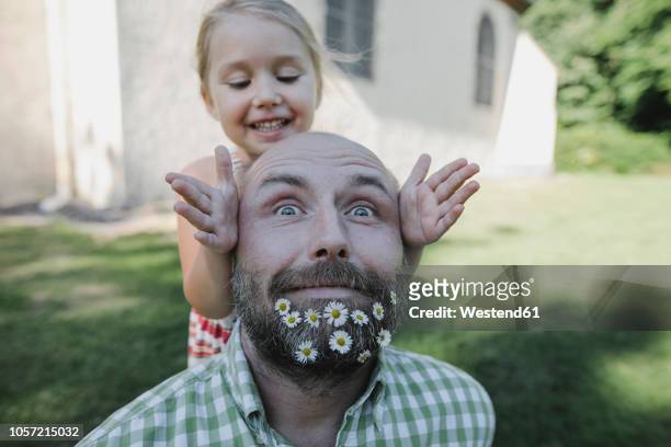 portrait of mature man with daisies in his beard playing with little daughter in the garden - caretas - fotografias e filmes do acervo