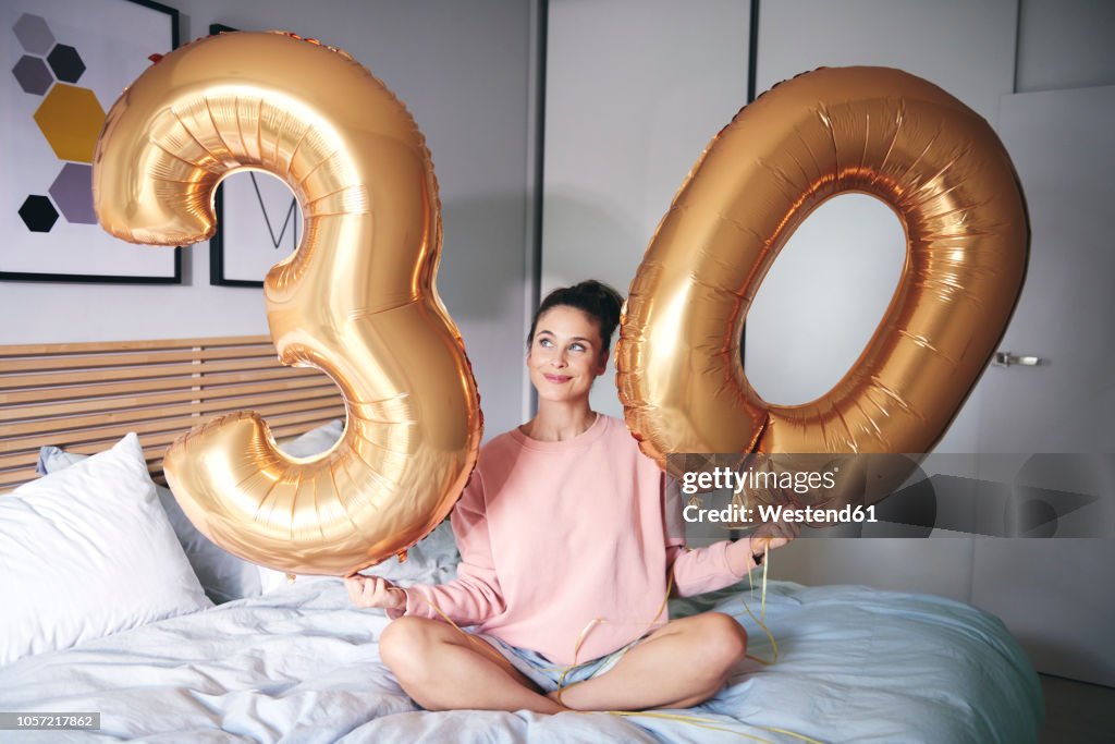 Happy woman holding golden balloons at birthday morning