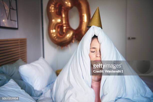 sad woman celebrating her birthday, sitting on bed under blanket - coprire foto e immagini stock