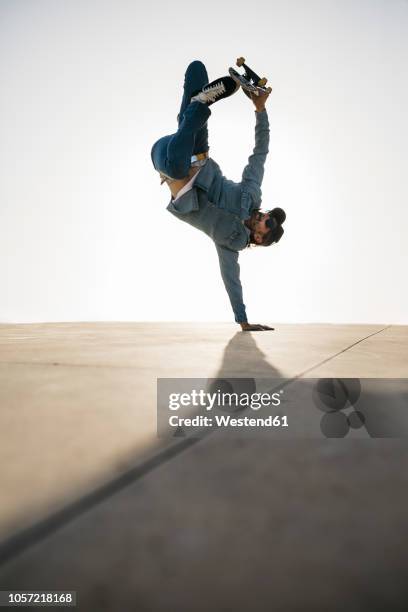 stylish man in denim outfit showing trick with skate in handstand - ハーフパイプ ストックフォトと画像