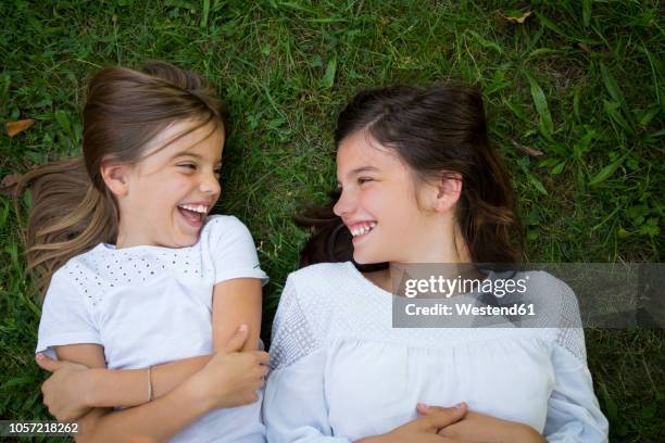 two sisters lying together on a meadow having fun - happy tween girls lying on grass stock pictures, royalty-free photos & images