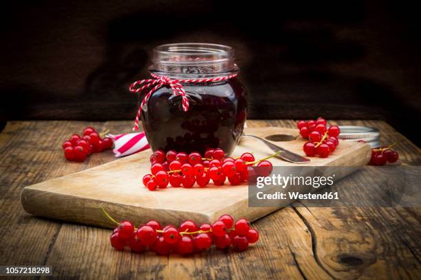 jam jar of currant jelly and red currants on wooden board - johannisbeere stock-fotos und bilder