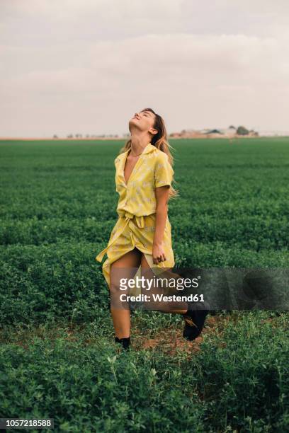 young woman walking in a green field - robe jaune photos et images de collection
