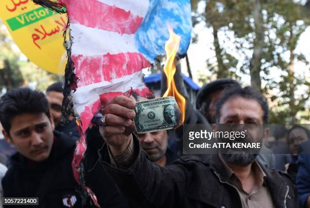 On the eve of renewed sanctions by Washington, An Iranian protester burns a dollar banknote during a demonstration outside the former US embassy in...