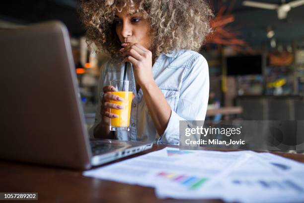 junge afrikanische frau online in einem café arbeiten konzentriert - drinking juice stock-fotos und bilder