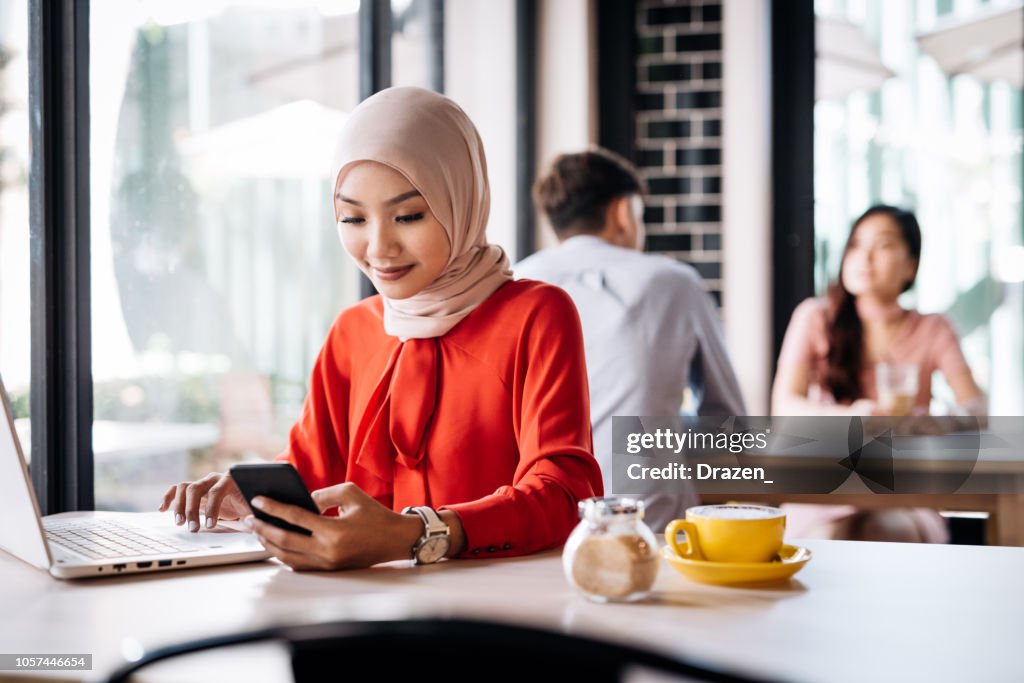 Malaysian woman in cafe using electronic banking on laptop