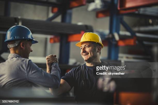 junge glückliche arbeiter und manager geben einander männlich grüßen am stahlwerk. - berufliche beschäftigung stock-fotos und bilder