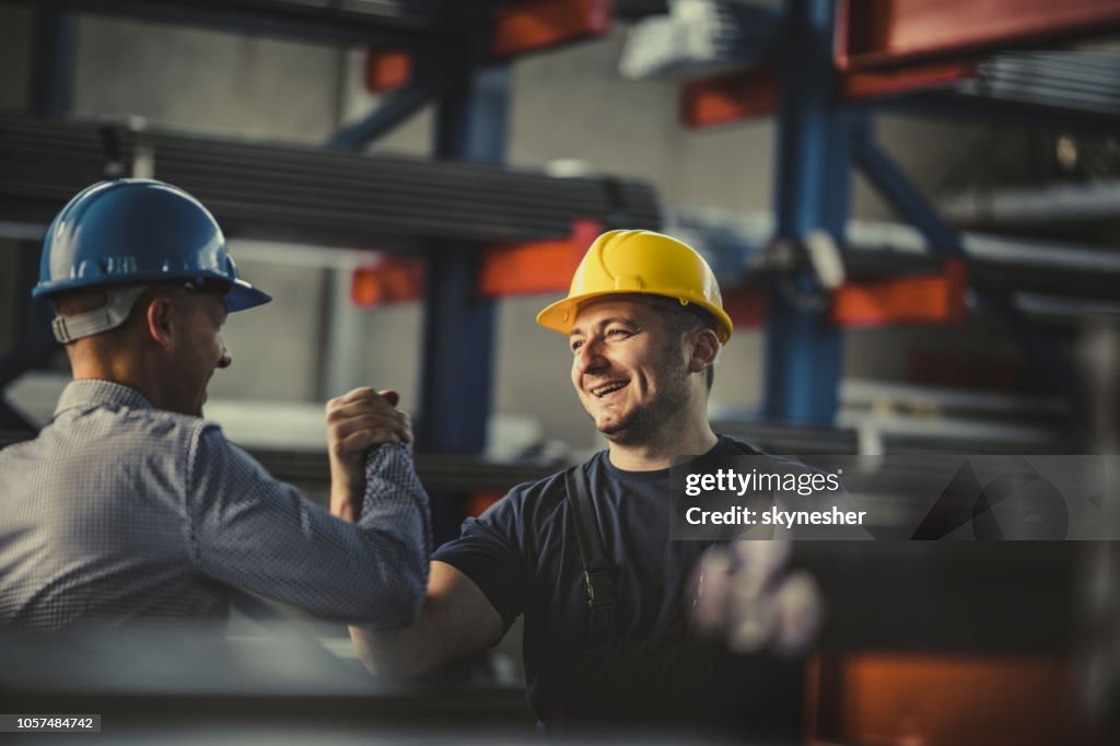 Young happy worker and manager giving each other manly greet at steel mill.
