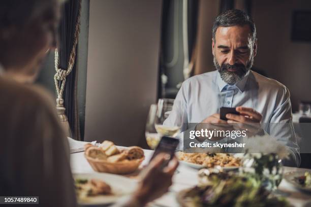 smiling senior man using cell phone on a lunch with his wife. - rudeness stock pictures, royalty-free photos & images